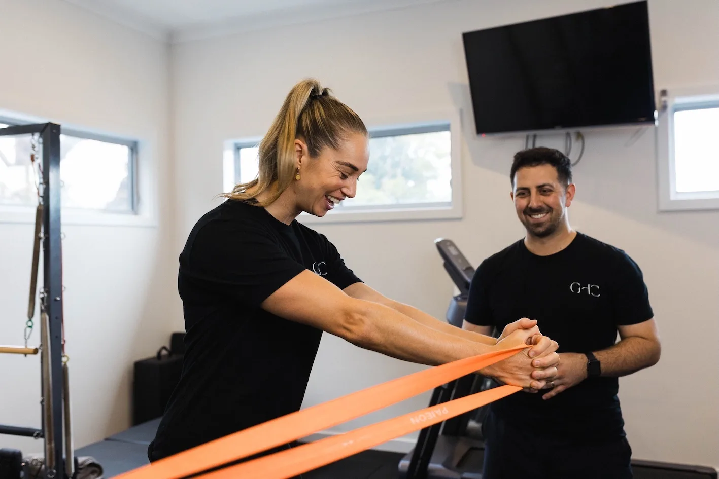 A Gladesville Healthcare exercise physiologist smiling as a colleague works through a resistance band exercise