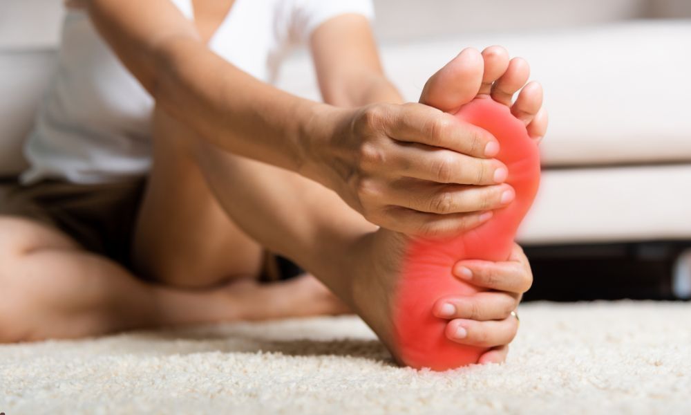 A person sits on the floor holding a red, painful foot—chiropractic care for back pain can help.