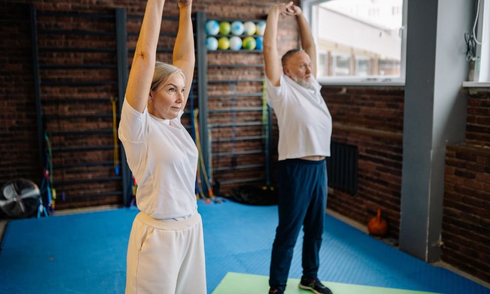Two older adults stretch in a gym, promoting remedial massage for muscle tension relief.
